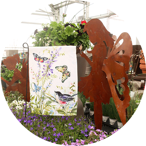 A white garden flag with butterflies and birds on it next to a fairy garden art statue.